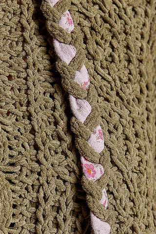 Close-up of a chunky knit garment in olive green, featuring a braided decorative trim with light pink and white floral fabric.