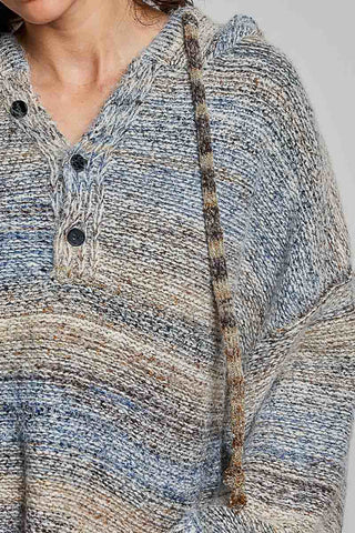 Close-up of a person wearing a chunky knit pullover sweater with a V-neck and dark buttons. The sweater has a marled, heathered texture in muted blue, beige, gray, and brown tones, with a matching striped drawstring.