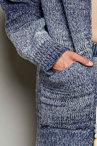 Close-up of a person wearing a marled blue and gray knit cardigan with a pocket, with a hand tucked into the side pocket.