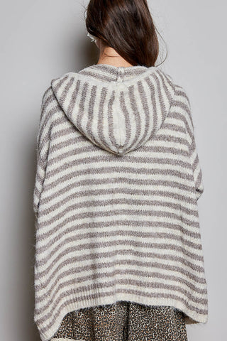A person shown from the back wearing a fuzzy knit hooded poncho with horizontal beige and gray stripes, photographed against a plain light gray wall.