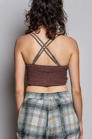 Back view of a woman wearing a brown smocked halter crop top with crisscross braided straps and plaid pants against a gray background.