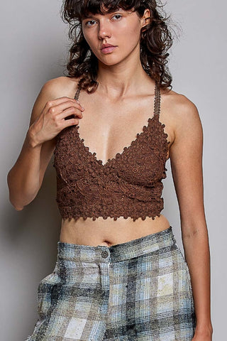 A woman wearing a brown lace halter crop top and a blue-gray plaid skirt, posing against a neutral gray background.