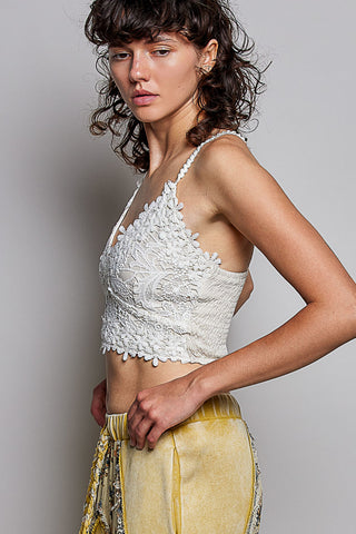 A model wearing a white lace halter crop top with pom-pom trim and yellow velvet pants, photographed against a neutral gray studio background.