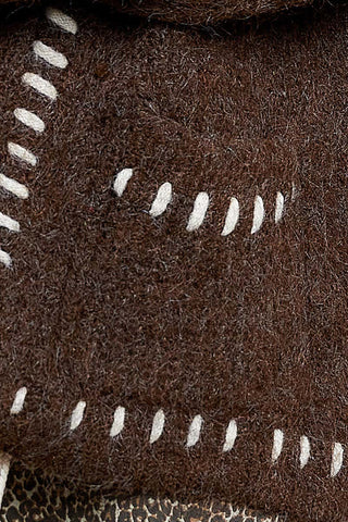 Close-up of a dark brown textured fabric with white whipstitching along the edges.
