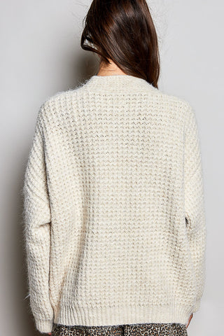A person shown from the back wearing a chunky knit cream-colored sweater against a plain light gray background.