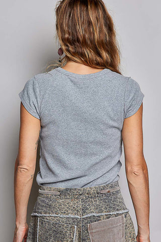 A woman viewed from behind wearing a heather gray short-sleeve t-shirt and patterned leopard-print pants against a plain light gray background.