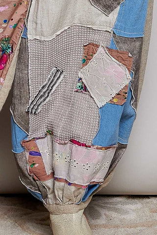 A close-up of a patchwork fabric garment, likely a skirt or pants leg, featuring a mix of blue denim, beige tweed, pink floral fabric, and striped textile panels, shown on a mannequin against a neutral background.