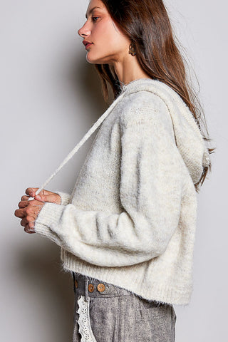 A woman wearing a fuzzy off-white cropped hoodie sweater, shown in profile against a plain light gray background.