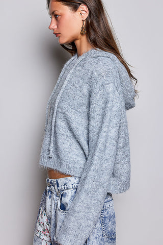 A woman shown in side profile wearing a light blue-gray fuzzy cropped hoodie and light-wash denim jeans against a plain light gray studio background.