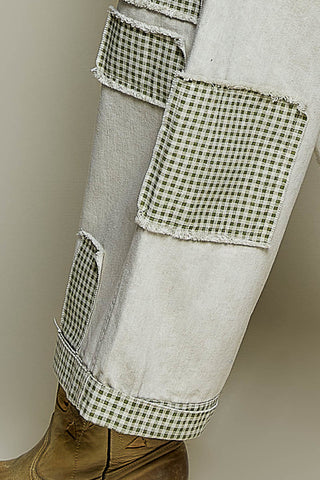 Close-up of a pair of light gray or off-white denim jeans with large green-and-white gingham patch pockets and a matching gingham hem trim, shown on a mannequin leg with a brown boot visible at the bottom.