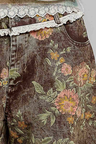 Close-up of a pair of dark brown velvet jeans featuring a pink and yellow floral print, decorated with white lace trim at the waistband.