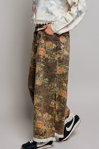 A person wearing wide-leg brown corduroy pants with a vintage floral print, a cream knit sweater with lace trim, and black Nike sneakers with white lace trim, shown from the waist down against a neutral gray background.