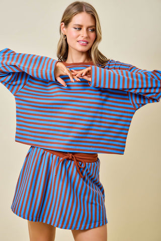 Woman wearing a blue and brown striped outfit against a beige background