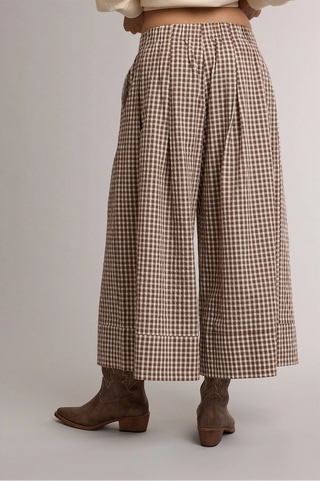 Brown and beige gingham wide-leg cropped pants shown on a model from the back, paired with brown leather ankle boots against a neutral studio background.