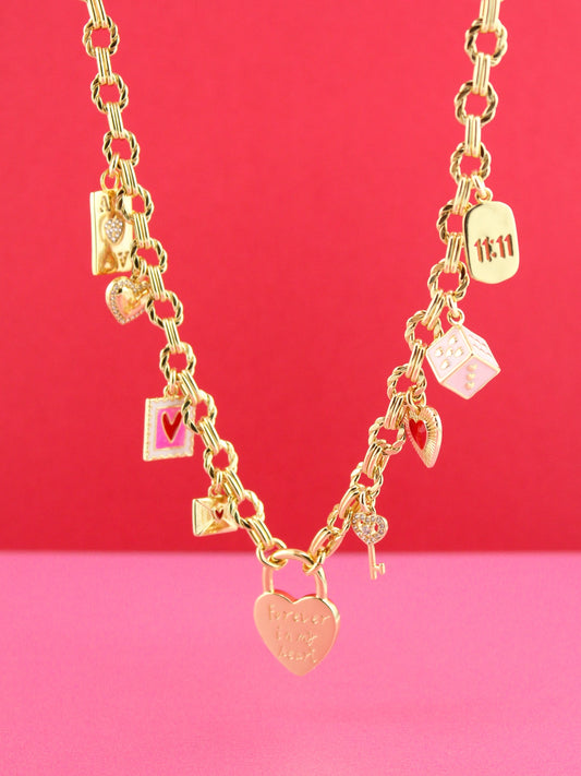 Gold necklace with various charms on a pink and red gradient background