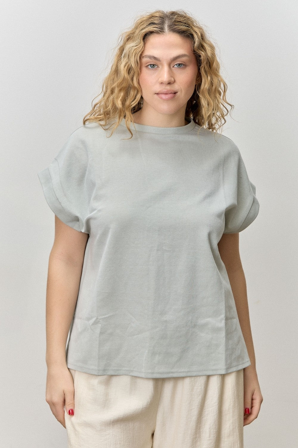 Woman wearing a light gray top and beige pants against a plain background