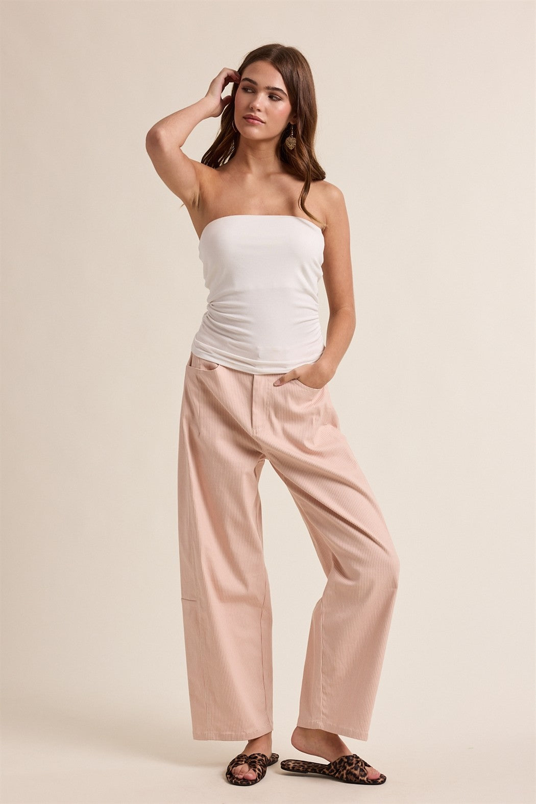 Woman wearing a white strapless top and pink pants on a beige background