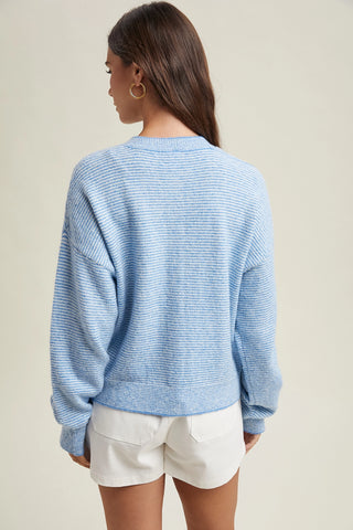 Woman wearing a light blue sweater and white shorts on a plain background
