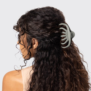 Woman with long, wavy hair using a hair tie against a plain background