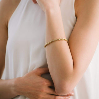 Close-up of a person wearing a gold bracelet on a plain background