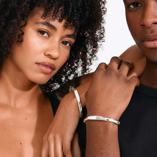 Two models wearing slim silver bangle bracelets against a clean white background.