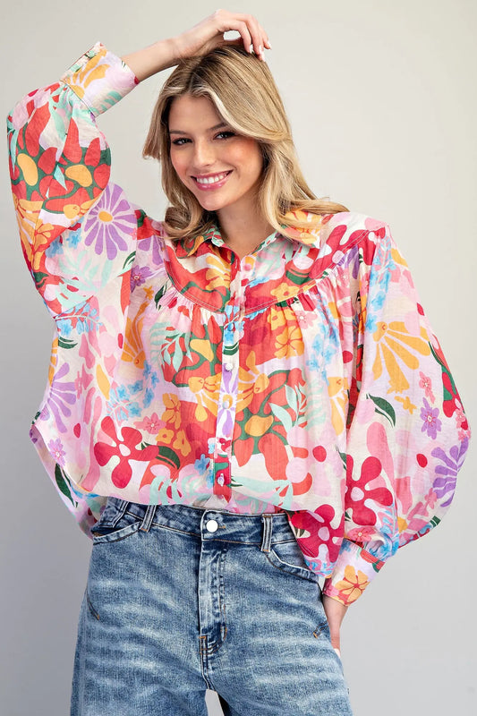 Woman wearing a colorful floral blouse and jeans against a plain background
