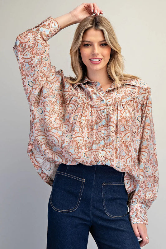 Woman wearing a floral blouse and dark jeans against a plain background