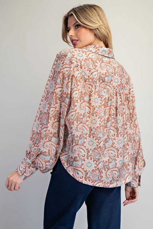 Woman wearing a patterned blouse and dark pants against a plain background