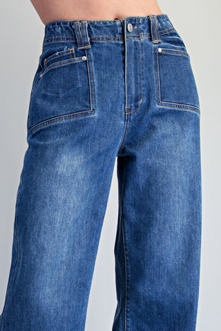 Close-up of a person wearing blue denim jeans, showing the back waistband, belt loops, back pockets, and upper legs against a light gray studio background.