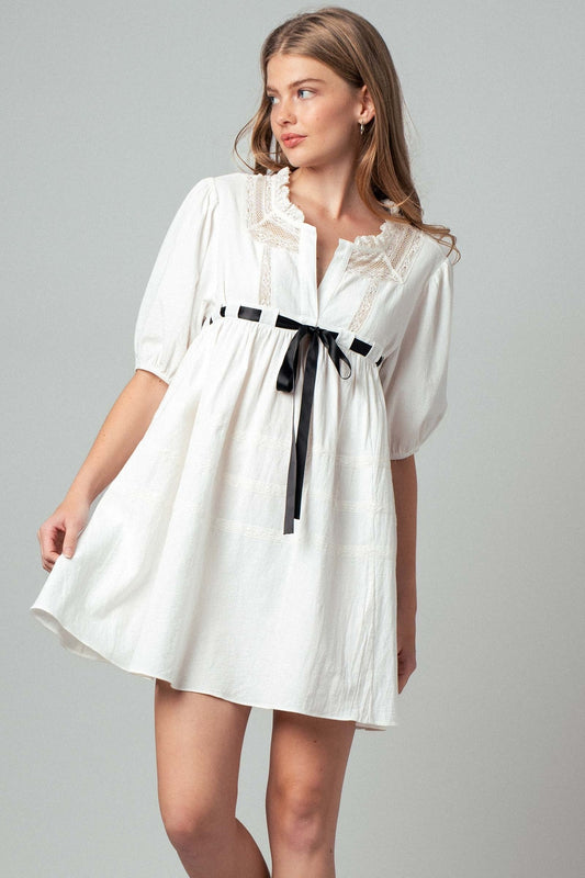 Woman wearing a white dress with a black belt on a gray background