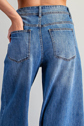 Close-up back view of a person wearing blue denim jeans with a hand in the back pocket, shown against a light gray studio background.