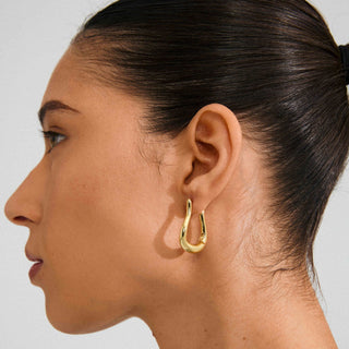 Woman wearing a gold hoop earring against a neutral background