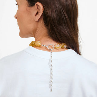 A close-up back view of a woman wearing a beaded choker necklace with yellow marbled beads and a silver-toned ring clasp with a dangling chain.