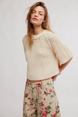Woman wearing a cream knitted top and floral pants on a white background