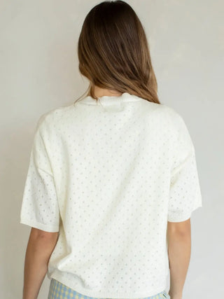 Woman wearing a white blouse with a subtle pattern against a plain background