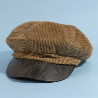 Brown corduroy cap with leather visor on a light blue background