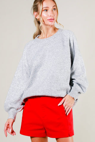 Woman wearing a gray sweater and red shorts against a plain background