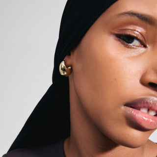 Close-up of a woman wearing gold hoop earrings with a neutral background