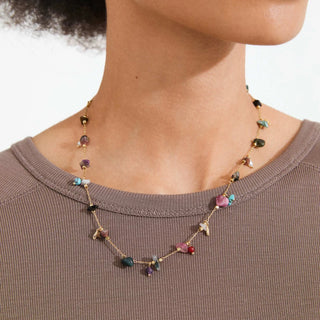 Necklace with multicolored stones worn by a person on a plain background