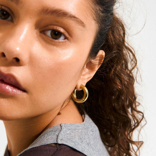 Close-up of a woman wearing gold hoop earrings with a neutral background