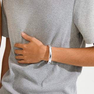 Person wearing a gray t-shirt with a hand on the back, wearing a silver bracelet.