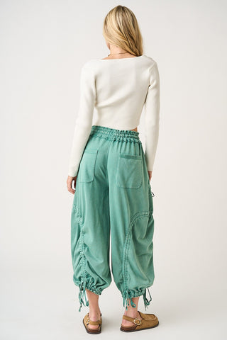 Person wearing teal baggy pants and a white long-sleeve shirt on a white background