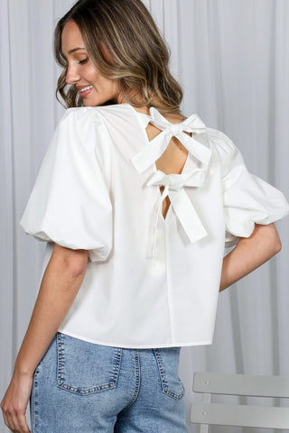 Woman wearing a white blouse with bow details and blue jeans against a light background