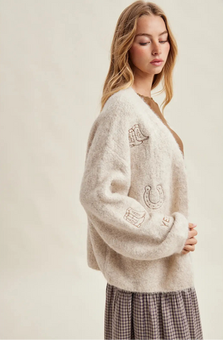 Woman wearing a cream-colored sweater with embroidered designs on a plain background