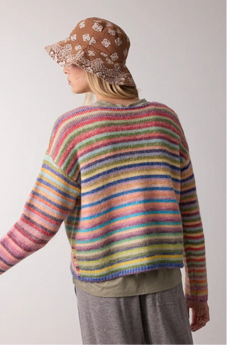 A women wearing a rainbow sweater against a neutral background.
