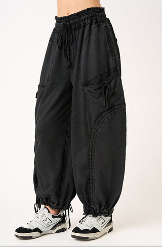 Black baggy cargo pants with an elastic drawstring waist and elastic cuffs, shown on a model wearing white and black sneakers against a light studio background.