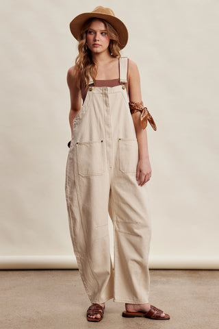 Woman wearing beige overalls and a hat on a plain background