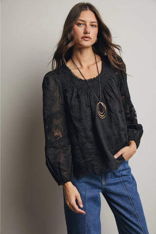 Woman wearing a black lace top and blue jeans against a neutral background