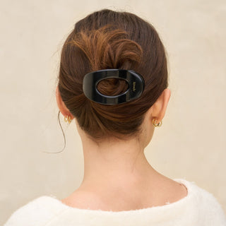 Person with a black hair clip in their bun against a beige background