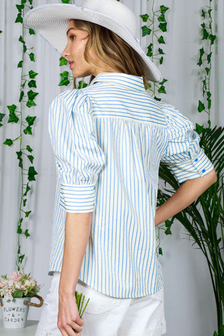Woman wearing a white and blue striped shirt with a white hat, standing against a white background with greenery.